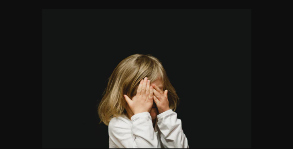 Una bambina si copre il viso con le mani