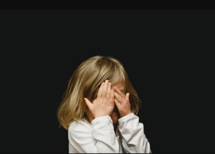 Una bambina si copre il viso con le mani
