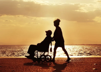 Un disabile viene spinto su una carrozzella, al mare